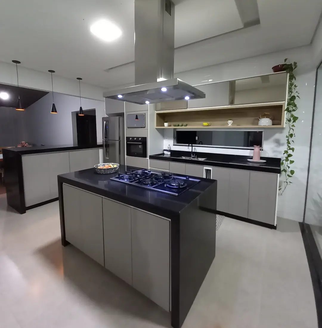 Cozinha com ilha preta, cooktop e coifa inox, armários claros e nicho de madeira