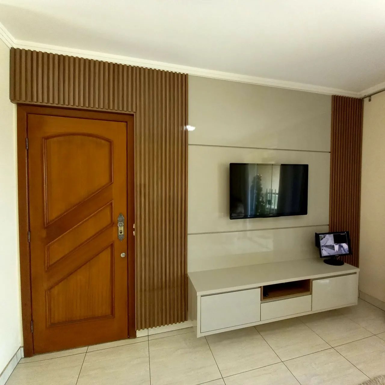 Sala com ripado de madeira dos dois lados da porta e rack branco suspenso